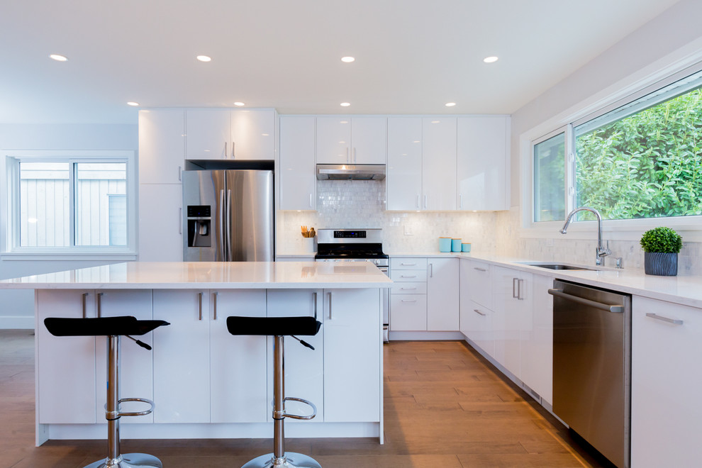 Modern inredning av ett stort kök, med en undermonterad diskho, släta luckor, vita skåp, bänkskiva i kvarts, vitt stänkskydd, stänkskydd i stenkakel, rostfria vitvaror, mellanmörkt trägolv och en köksö