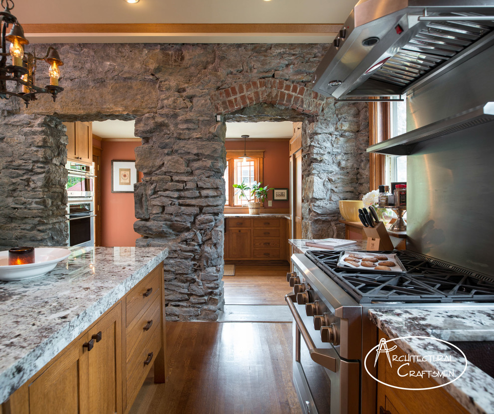 Example of a mountain style kitchen design in Kansas City with a farmhouse sink, shaker cabinets, medium tone wood cabinets, granite countertops and paneled appliances
