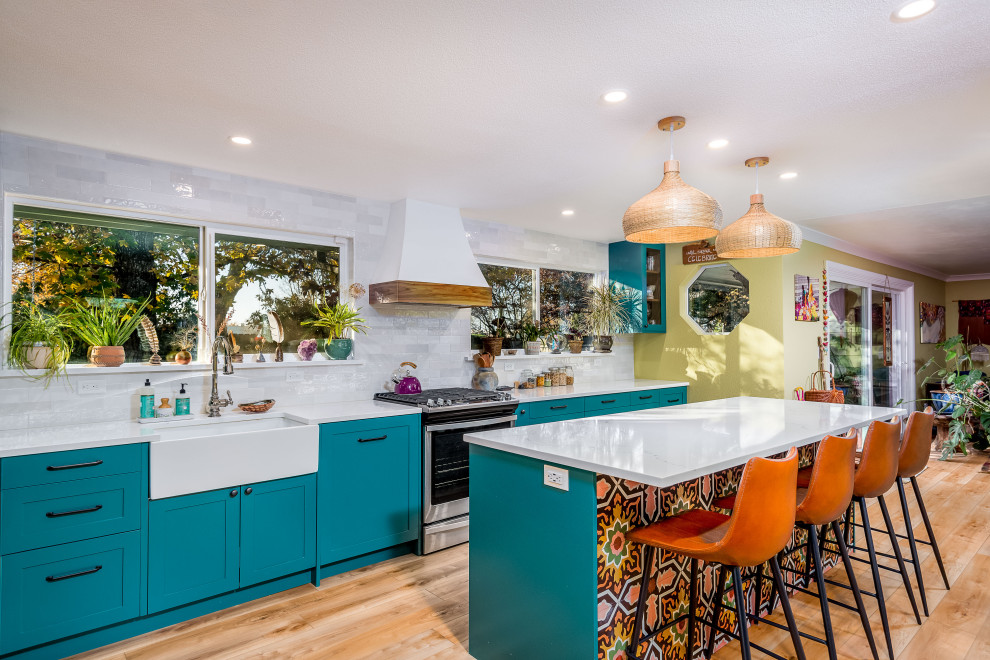 Large island style galley light wood floor and beige floor open concept kitchen photo in Portland with a farmhouse sink, shaker cabinets, blue cabinets, gray backsplash, subway tile backsplash, an island, white countertops, solid surface countertops and stainless steel appliances