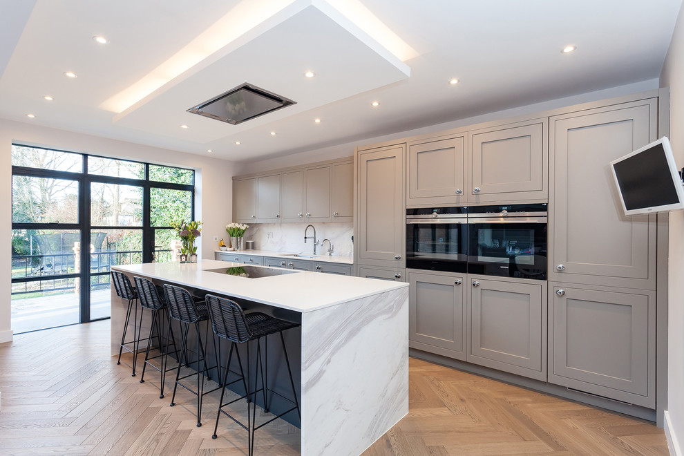 Idée de décoration pour une cuisine américaine linéaire, encastrable et bicolore design de taille moyenne avec un évier intégré, un placard à porte shaker, des portes de placard grises, un plan de travail en quartz, une crédence blanche, une crédence en marbre et îlot.