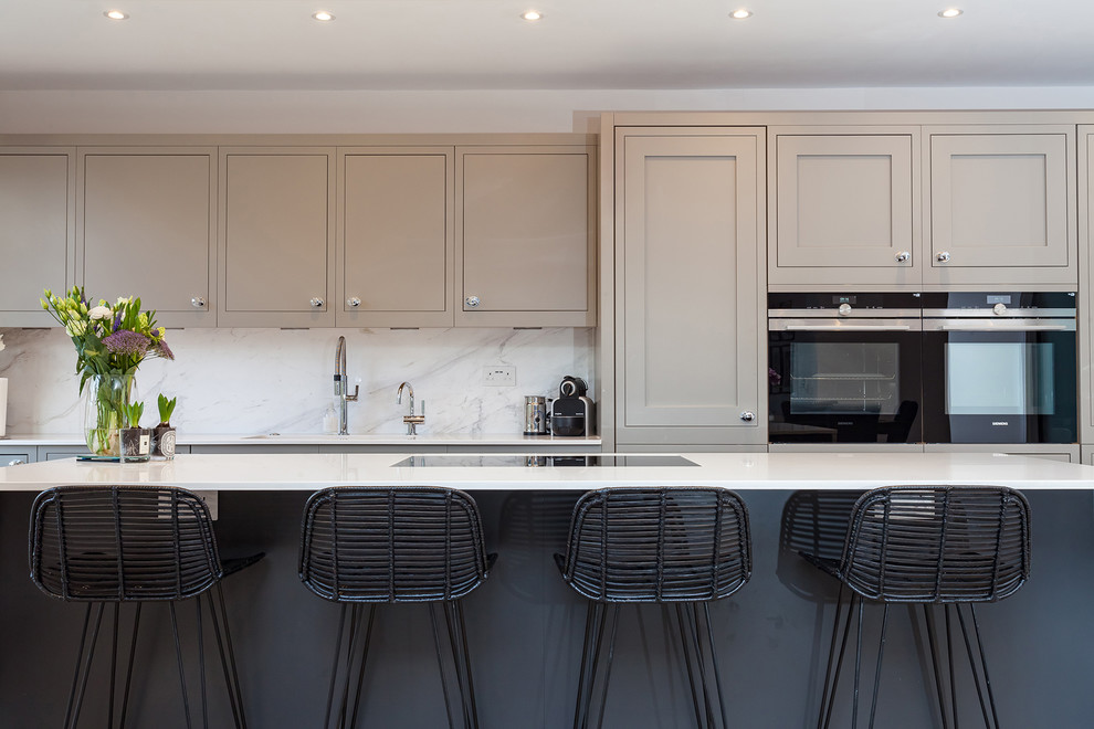 Ejemplo de cocina comedor lineal, clásica, de tamaño medio, con fregadero integrado, armarios estilo shaker, puertas de armario grises, encimera de cuarcita, salpicadero blanco, salpicadero de mármol, electrodomésticos con paneles y una isla