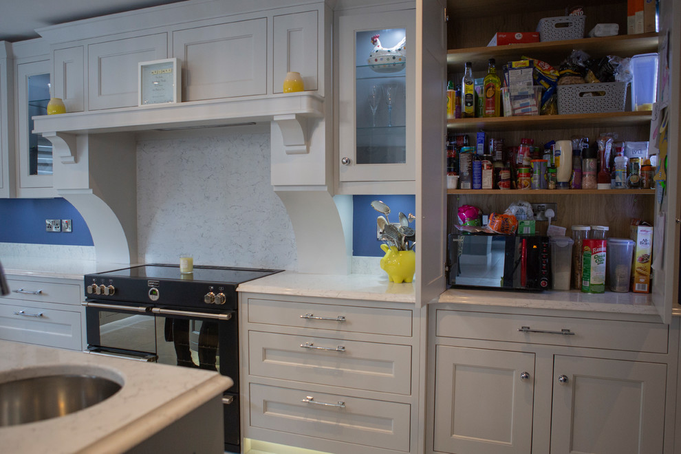 Klassisk inredning av ett stort vit vitt kök, med en integrerad diskho, luckor med profilerade fronter, grå skåp, bänkskiva i kvartsit, vitt stänkskydd, stänkskydd i sten, rostfria vitvaror, klinkergolv i porslin, en köksö och grått golv