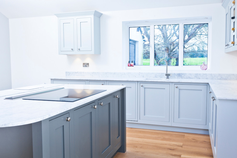 Large cottage light wood floor open concept kitchen photo in Buckinghamshire with a double-bowl sink, shaker cabinets, gray cabinets, marble countertops, black appliances and an island