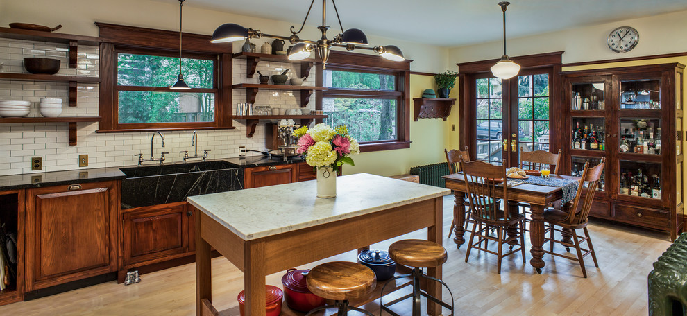 Eat-in kitchen - huge craftsman l-shaped light wood floor eat-in kitchen idea in Portland with an integrated sink, raised-panel cabinets, medium tone wood cabinets, soapstone countertops, white backsplash, subway tile backsplash, black appliances and an island