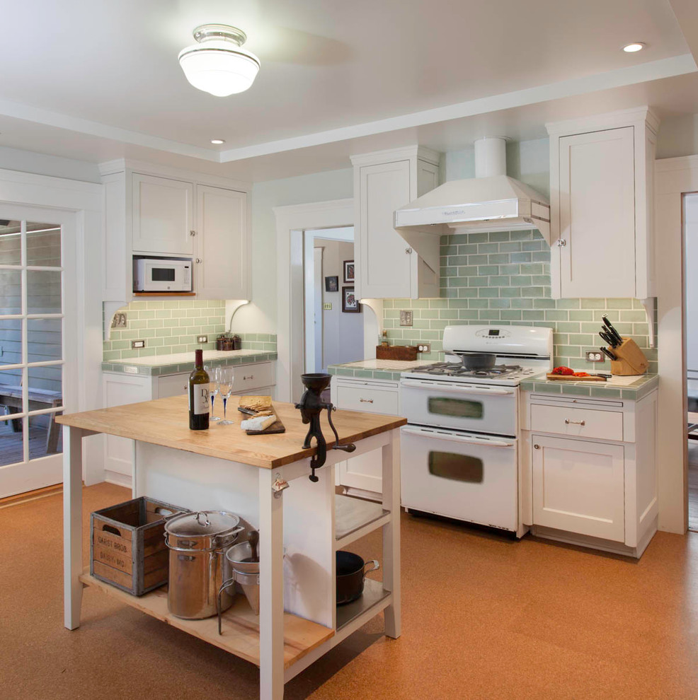 Design ideas for a classic enclosed kitchen in San Diego with a submerged sink, shaker cabinets, white cabinets, tile countertops, green splashback, ceramic splashback, white appliances, cork flooring, an island and brown floors.