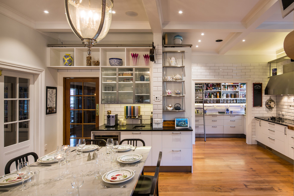 Large urban l-shaped kitchen/diner in Wellington with a submerged sink, glass-front cabinets, white cabinets, granite worktops, white splashback, ceramic splashback, stainless steel appliances, medium hardwood flooring and an island.