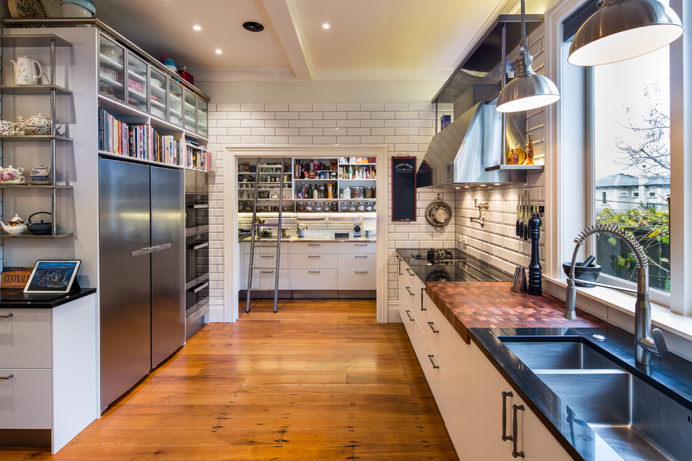 Photo of a large industrial l-shaped kitchen/diner in Wellington with a submerged sink, glass-front cabinets, white cabinets, granite worktops, white splashback, ceramic splashback, stainless steel appliances, medium hardwood flooring and an island.