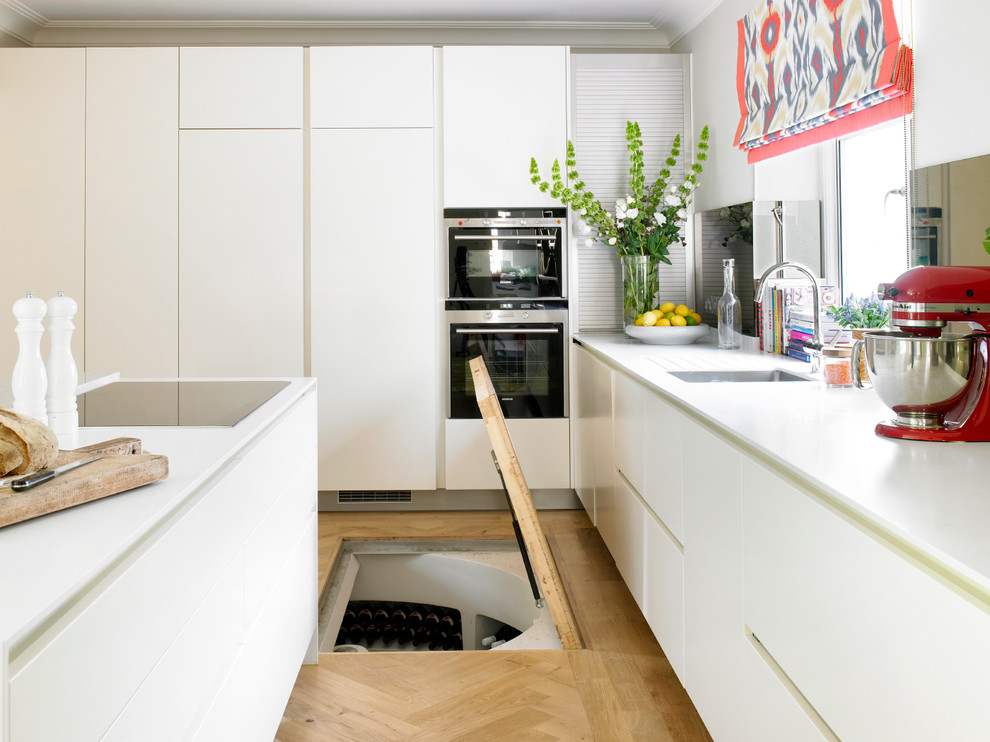 Modern inredning av ett mellanstort kök, med en undermonterad diskho, släta luckor, vita skåp, integrerade vitvaror, ljust trägolv och en köksö