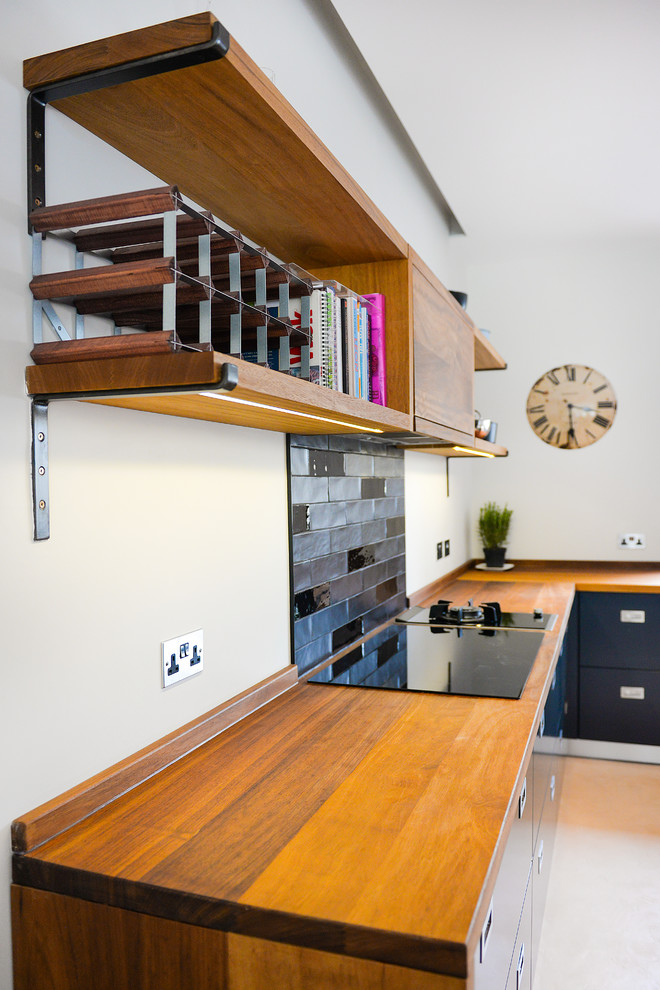 Bild på ett stort funkis kök med öppen planlösning, med en nedsänkt diskho, släta luckor, blå skåp, träbänkskiva, svart stänkskydd, stänkskydd i keramik, svarta vitvaror, betonggolv och en köksö