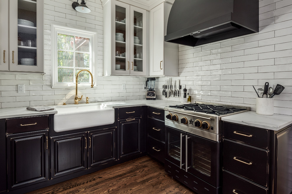 This is an example of a medium sized country u-shaped enclosed kitchen in Tampa with a belfast sink, raised-panel cabinets, black cabinets, marble worktops, white splashback, metro tiled splashback, stainless steel appliances, medium hardwood flooring, no island, brown floors and white worktops.