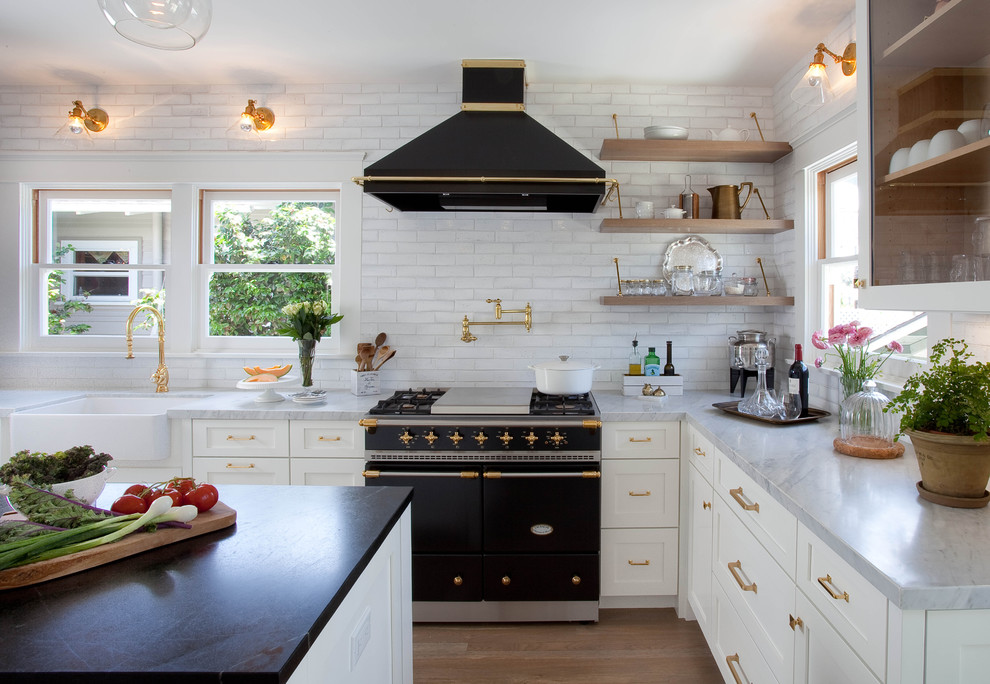 Transitional u-shaped medium tone wood floor kitchen photo in San Diego with a farmhouse sink, shaker cabinets, white cabinets, white backsplash, black appliances and an island