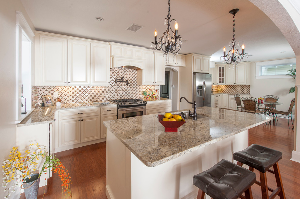 This is an example of a large traditional l-shaped kitchen/diner in Tampa with a double-bowl sink, raised-panel cabinets, light wood cabinets, granite worktops, multi-coloured splashback, ceramic splashback, stainless steel appliances, dark hardwood flooring, an island and brown floors.