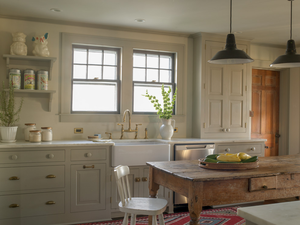 Inredning av ett lantligt kök, med en rustik diskho, grå skåp, marmorbänkskiva, grått stänkskydd, rostfria vitvaror och en köksö