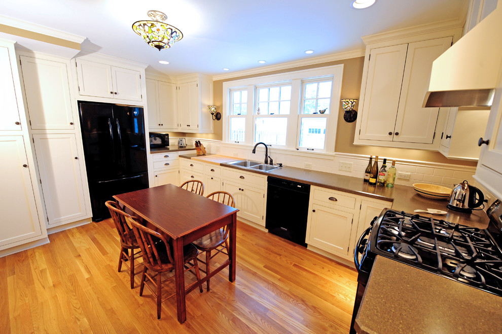 Example of a mid-sized classic u-shaped medium tone wood floor and brown floor enclosed kitchen design in Cleveland with a double-bowl sink, recessed-panel cabinets, white cabinets, laminate countertops, white backsplash, subway tile backsplash, black appliances and no island