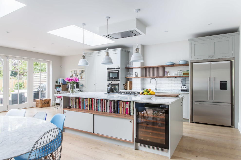 Moderne Wohnküche mit Schrankfronten im Shaker-Stil, grauen Schränken, Marmor-Arbeitsplatte, Küchenrückwand in Weiß, Küchengeräten aus Edelstahl, hellem Holzboden, Kücheninsel und Rückwand aus Metrofliesen in London