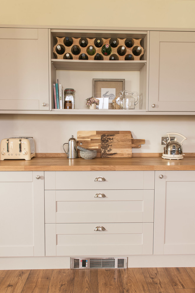 Mid-sized country laminate floor and brown floor eat-in kitchen photo in Sussex with a farmhouse sink, shaker cabinets, beige cabinets, wood countertops, white backsplash, porcelain backsplash, stainless steel appliances, a peninsula and brown countertops