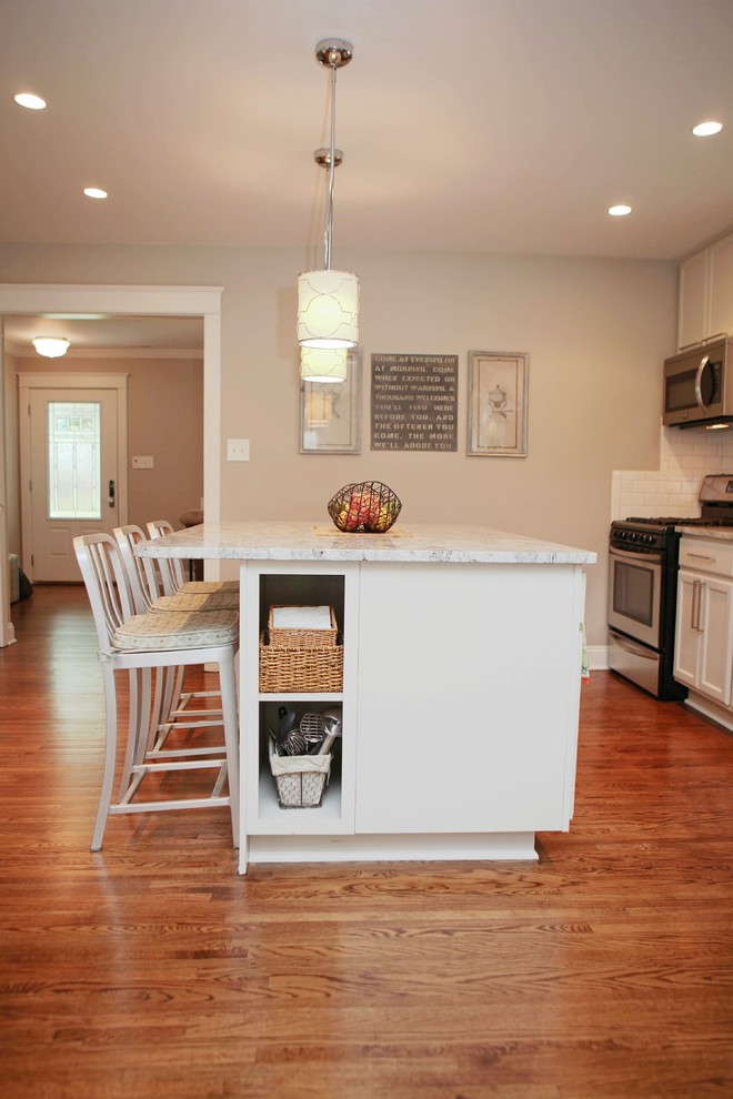 Ejemplo de cocina lineal moderna con salpicadero blanco, salpicadero de azulejos tipo metro, electrodomésticos de acero inoxidable, suelo de madera en tonos medios y una isla