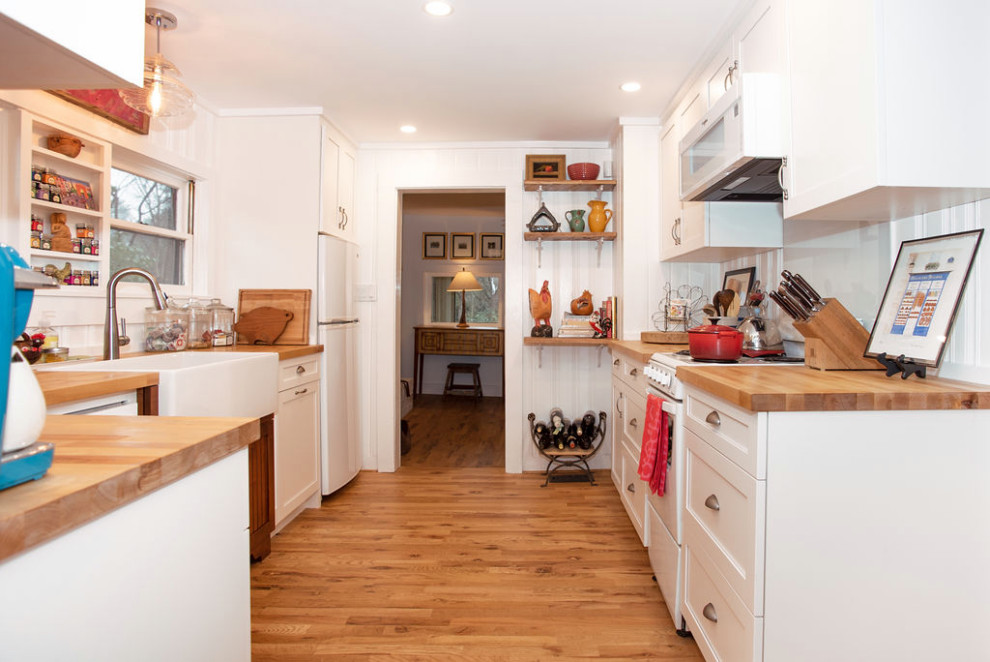 Enclosed kitchen - small shabby-chic style galley light wood floor and brown floor enclosed kitchen idea in Other with a farmhouse sink, shaker cabinets, white cabinets, wood countertops, white backsplash, glass sheet backsplash, white appliances, no island and brown countertops
