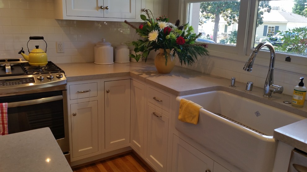 Example of a mid-sized classic u-shaped light wood floor eat-in kitchen design in Santa Barbara with a farmhouse sink, recessed-panel cabinets, white cabinets, quartz countertops, white backsplash, cement tile backsplash, stainless steel appliances and an island