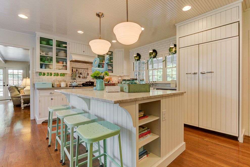 Cette photo montre une cuisine encastrable romantique en L avec des portes de placard blanches, une crédence blanche, une crédence en carrelage métro, un sol en bois brun et îlot.