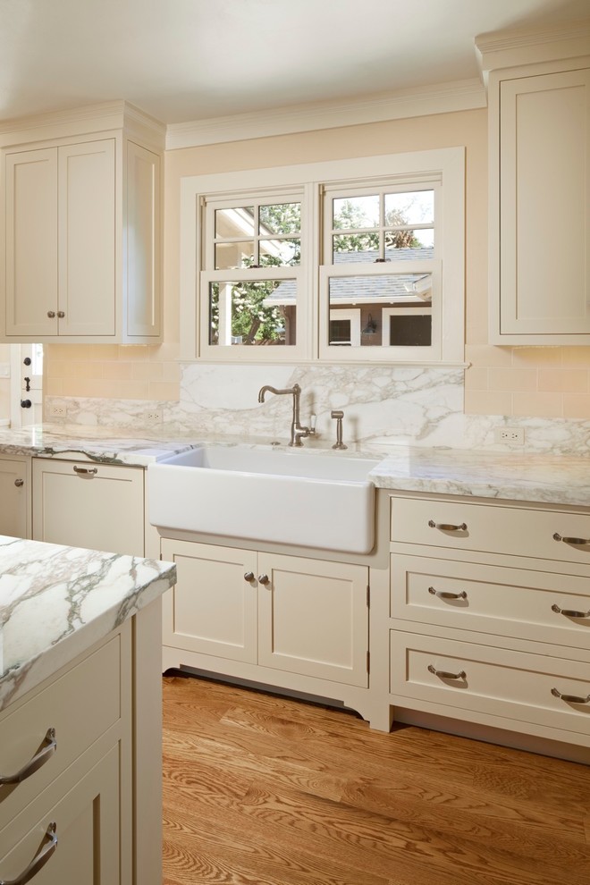 Inredning av ett klassiskt stort kök, med en rustik diskho, luckor med upphöjd panel, vita skåp, marmorbänkskiva, vitt stänkskydd, stänkskydd i marmor, rostfria vitvaror, ljust trägolv och en köksö