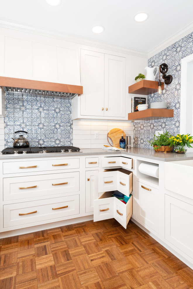 This is an example of a small eclectic l-shaped kitchen pantry in Other with a belfast sink, beaded cabinets, white cabinets, engineered stone countertops, blue splashback, terracotta splashback, stainless steel appliances, medium hardwood flooring, a breakfast bar, brown floors and grey worktops.