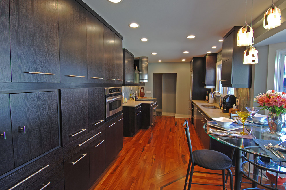Example of a large trendy galley medium tone wood floor eat-in kitchen design in Milwaukee with an undermount sink, flat-panel cabinets, dark wood cabinets, quartz countertops, multicolored backsplash, glass tile backsplash and stainless steel appliances