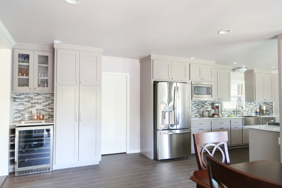 Example of a mid-sized transitional u-shaped porcelain tile and gray floor eat-in kitchen design in Other with a farmhouse sink, shaker cabinets, gray cabinets, quartz countertops, blue backsplash, glass sheet backsplash, stainless steel appliances and an island