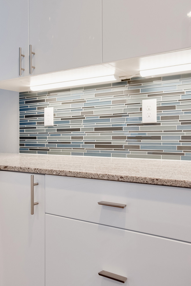 Medium sized contemporary u-shaped kitchen/diner in Minneapolis with a single-bowl sink, flat-panel cabinets, white cabinets, engineered stone countertops, blue splashback, glass tiled splashback, stainless steel appliances and medium hardwood flooring.