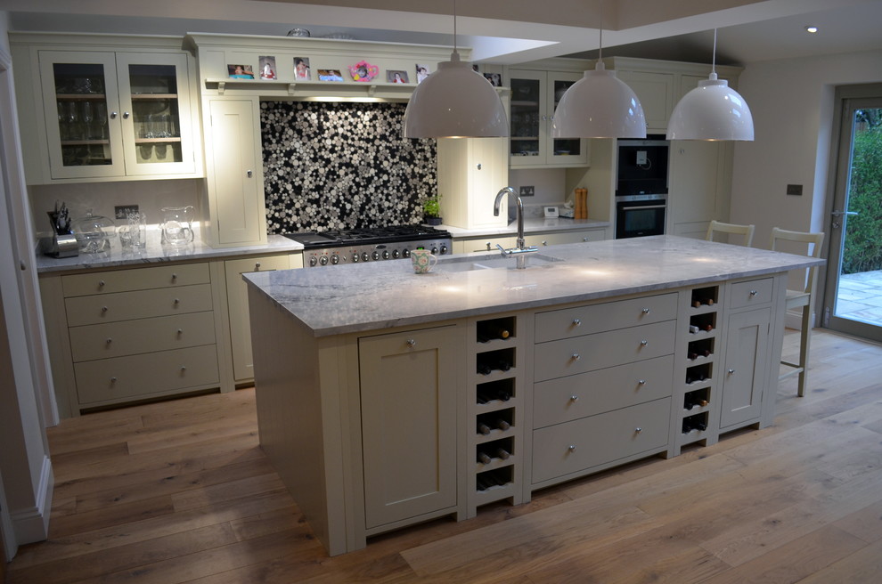 Inspiration for a medium sized contemporary single-wall kitchen/diner in Hertfordshire with a belfast sink, beaded cabinets, white cabinets, composite countertops, black splashback, ceramic splashback, black appliances, an island and light hardwood flooring.