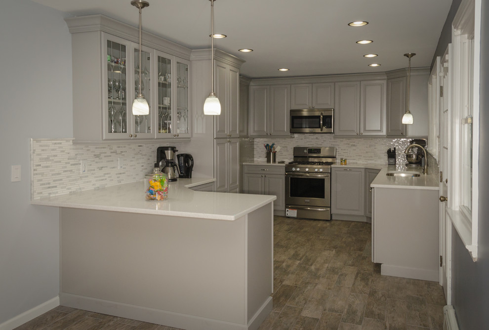 This is an example of a medium sized classic l-shaped kitchen/diner in New York with a submerged sink, raised-panel cabinets, grey cabinets, engineered stone countertops, grey splashback, ceramic splashback, stainless steel appliances, ceramic flooring, a breakfast bar and grey floors.