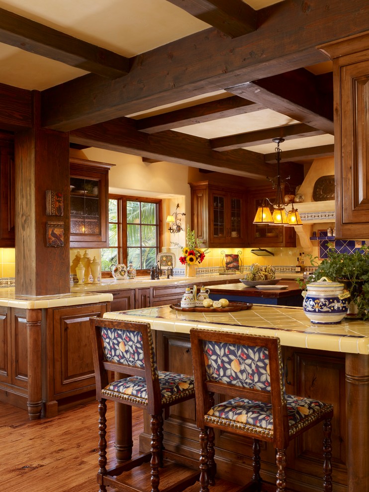 Example of a large tuscan u-shaped medium tone wood floor enclosed kitchen design in Phoenix with a double-bowl sink, raised-panel cabinets, medium tone wood cabinets, tile countertops, multicolored backsplash, ceramic backsplash, colored appliances and an island