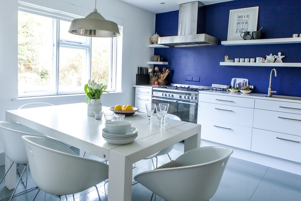 Beach style single-wall kitchen in Kent with flat-panel cabinets, white cabinets, composite countertops, stainless steel appliances, a submerged sink and a feature wall.