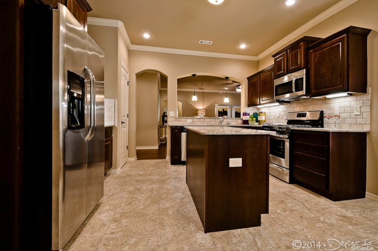 Foto de cocina comedor tradicional con fregadero de doble seno, armarios con paneles con relieve, puertas de armario de madera en tonos medios, encimera de granito, salpicadero beige, salpicadero de azulejos de piedra, electrodomésticos de acero inoxidable, suelo de baldosas de cerámica y una isla