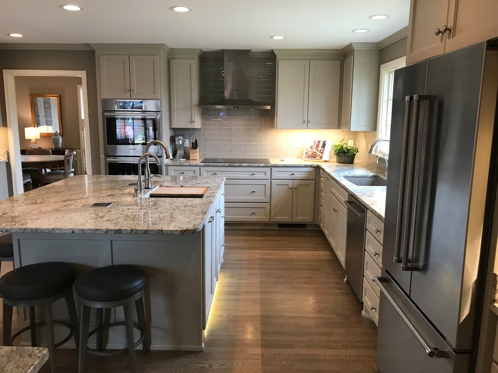 Large transitional l-shaped light wood floor and gray floor eat-in kitchen photo in Other with an undermount sink, shaker cabinets, gray cabinets, granite countertops, gray backsplash, glass tile backsplash, stainless steel appliances and an island