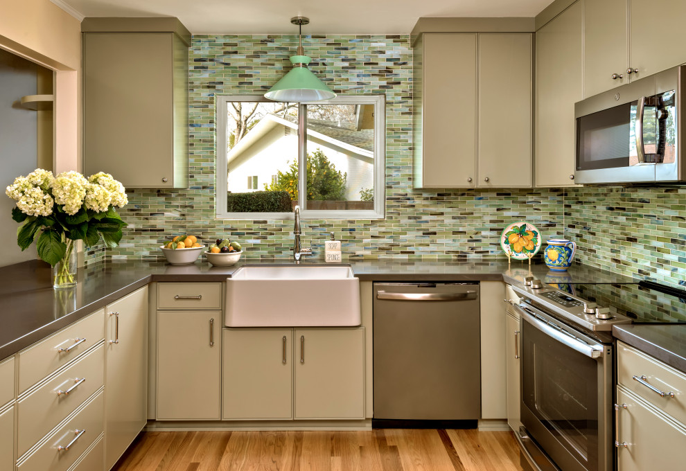 This is an example of a medium sized farmhouse l-shaped kitchen in San Francisco with a belfast sink, beaded cabinets, green cabinets, engineered stone countertops, green splashback, glass tiled splashback, light hardwood flooring, a breakfast bar and grey worktops.