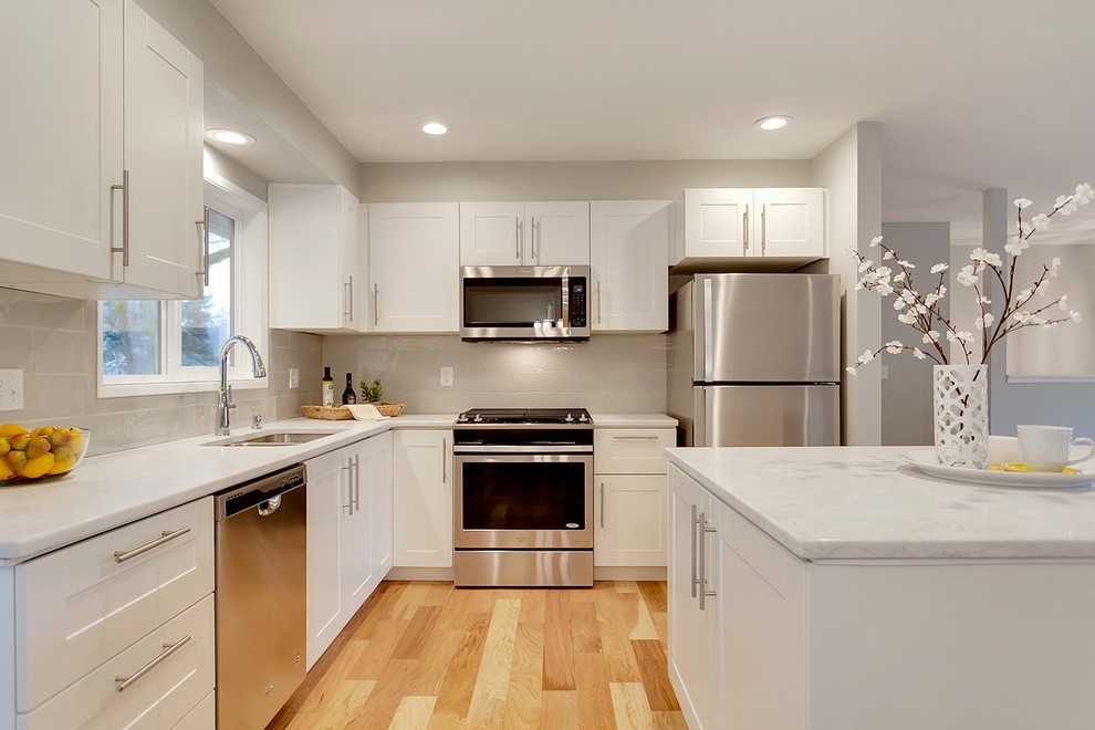 Foto på ett litet funkis kök, med en undermonterad diskho, skåp i shakerstil, vita skåp, bänkskiva i kvarts, grått stänkskydd, stänkskydd i tunnelbanekakel, rostfria vitvaror, mellanmörkt trägolv, en köksö och brunt golv