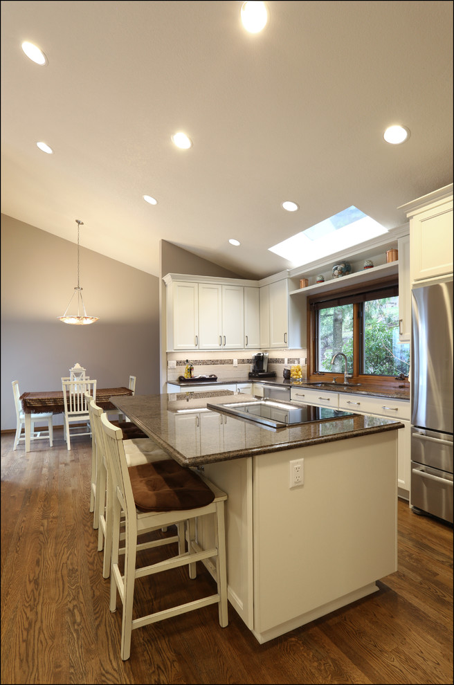 Mid-sized transitional medium tone wood floor and brown floor eat-in kitchen photo in Portland with an undermount sink, recessed-panel cabinets, white cabinets, granite countertops, brown backsplash, glass tile backsplash, stainless steel appliances, an island and brown countertops