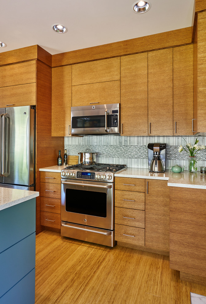 Bild på ett funkis kök och matrum, med en undermonterad diskho, släta luckor, skåp i mellenmörkt trä, bänkskiva i återvunnet glas, flerfärgad stänkskydd, stänkskydd i mosaik, rostfria vitvaror, bambugolv och en köksö
