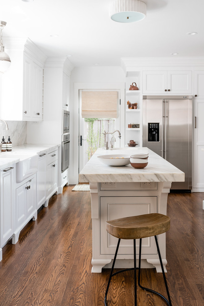 サクラメントにあるトランジショナルスタイルのおしゃれなキッチン (エプロンフロントシンク、白いキャビネット、シルバーの調理設備、無垢フローリング、茶色い床、白いキッチンカウンター) の写真
