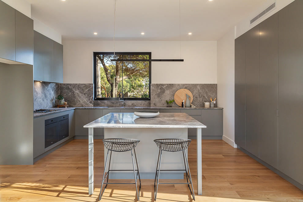 Foto på ett mellanstort funkis grå l-kök, med släta luckor, grå skåp, grått stänkskydd, stänkskydd i sten, ljust trägolv och en köksö