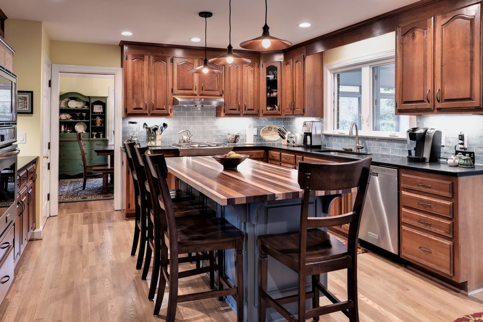 Klassisk inredning av ett stort u-kök, med en undermonterad diskho, luckor med upphöjd panel, skåp i mellenmörkt trä, grått stänkskydd, stänkskydd i tunnelbanekakel, rostfria vitvaror, mellanmörkt trägolv, en köksö och brunt golv