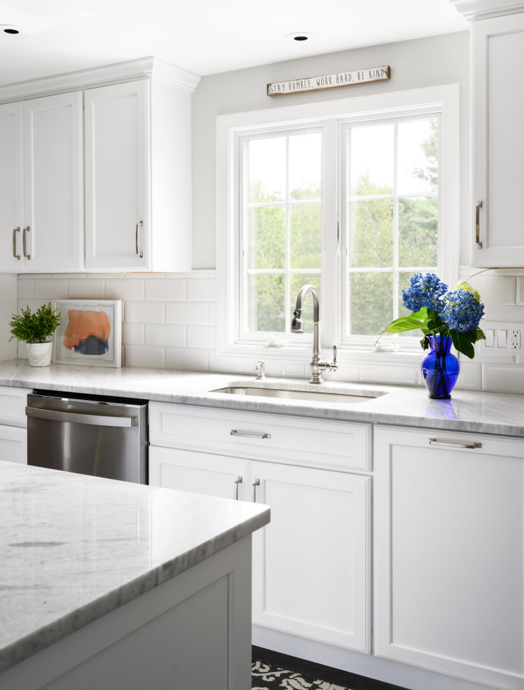 Inredning av ett klassiskt mellanstort vit vitt kök, med vita skåp, bänkskiva i kvartsit, vitt stänkskydd, stänkskydd i tunnelbanekakel, rostfria vitvaror, vinylgolv, en köksö och brunt golv