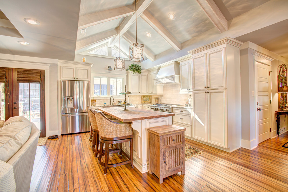 Eat-in kitchen - mid-sized traditional l-shaped bamboo floor eat-in kitchen idea in Other with a farmhouse sink, recessed-panel cabinets, white cabinets, wood countertops, white backsplash, subway tile backsplash, stainless steel appliances and an island