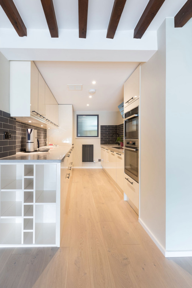 Mid-sized minimalist galley light wood floor and gray floor open concept kitchen photo in London with a drop-in sink, flat-panel cabinets, white cabinets, solid surface countertops, blue backsplash, porcelain backsplash, paneled appliances, no island and gray countertops