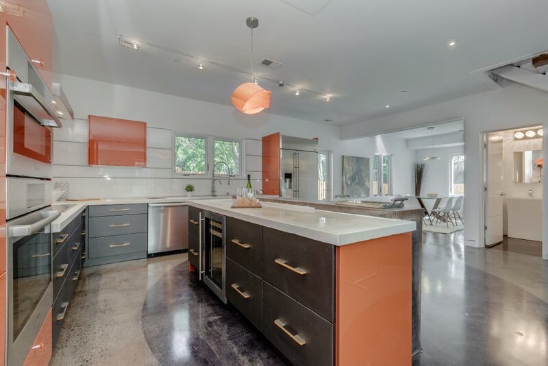 This is an example of a large contemporary single-wall open plan kitchen in DC Metro with flat-panel cabinets, orange cabinets, composite countertops, white splashback, glass sheet splashback, stainless steel appliances, concrete flooring and an island.