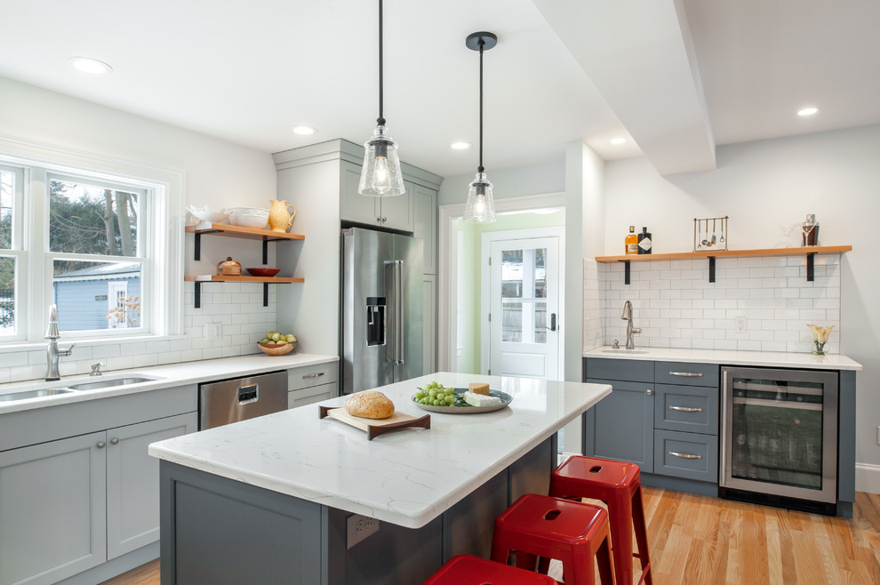 Inspiration for a large classic l-shaped kitchen in Detroit with a double-bowl sink, flat-panel cabinets, grey cabinets, white splashback, porcelain splashback, stainless steel appliances, medium hardwood flooring and an island.