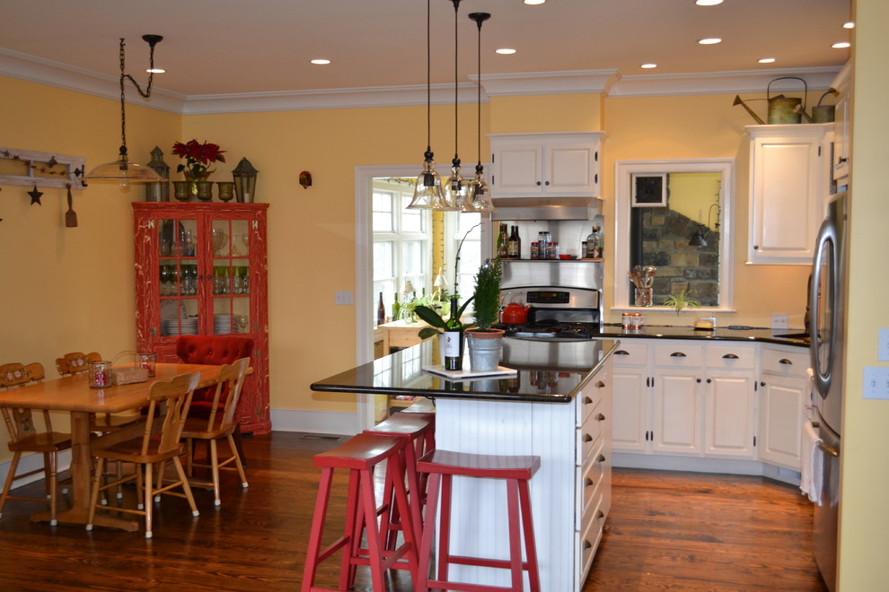 Große Landhausstil Wohnküche in L-Form mit Unterbauwaschbecken, profilierten Schrankfronten, gelben Schränken, Granit-Arbeitsplatte, Küchenrückwand in Gelb, Küchengeräten aus Edelstahl, dunklem Holzboden und Kücheninsel in Baltimore