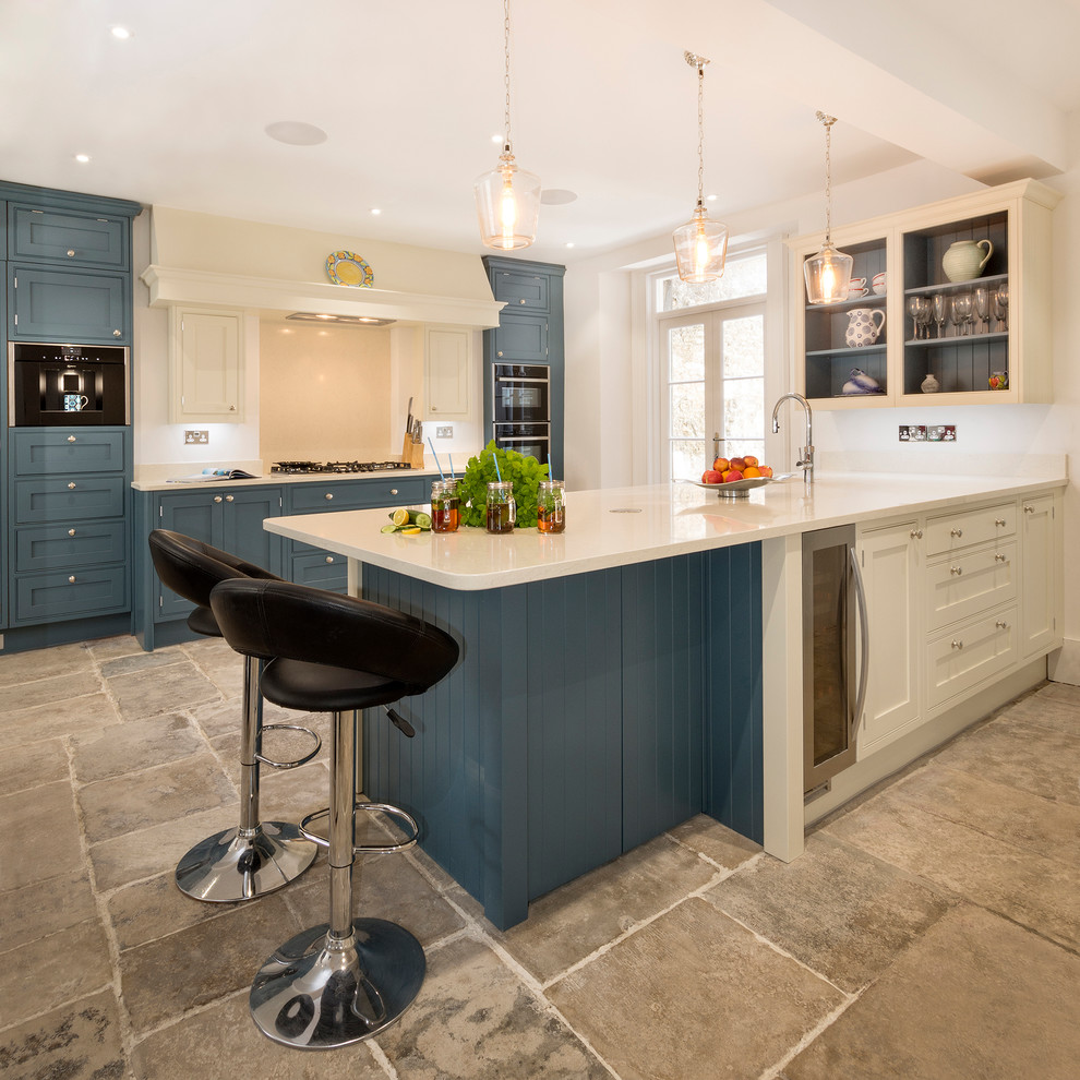 Große Klassische Küche mit Unterbauwaschbecken, Küchenrückwand in Beige, Küchengeräten aus Edelstahl, grauem Boden, weißer Arbeitsplatte, Schrankfronten im Shaker-Stil, blauen Schränken und Halbinsel in Cornwall