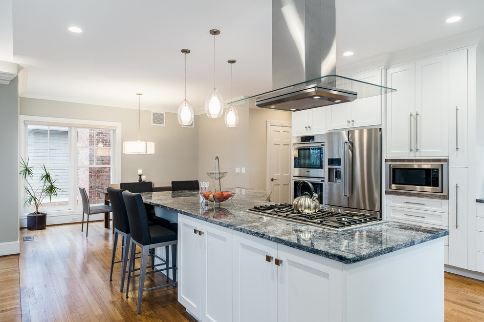 Open concept kitchen - large transitional l-shaped medium tone wood floor open concept kitchen idea in Bridgeport with an undermount sink, flat-panel cabinets, white cabinets, granite countertops, gray backsplash, glass tile backsplash, stainless steel appliances and an island